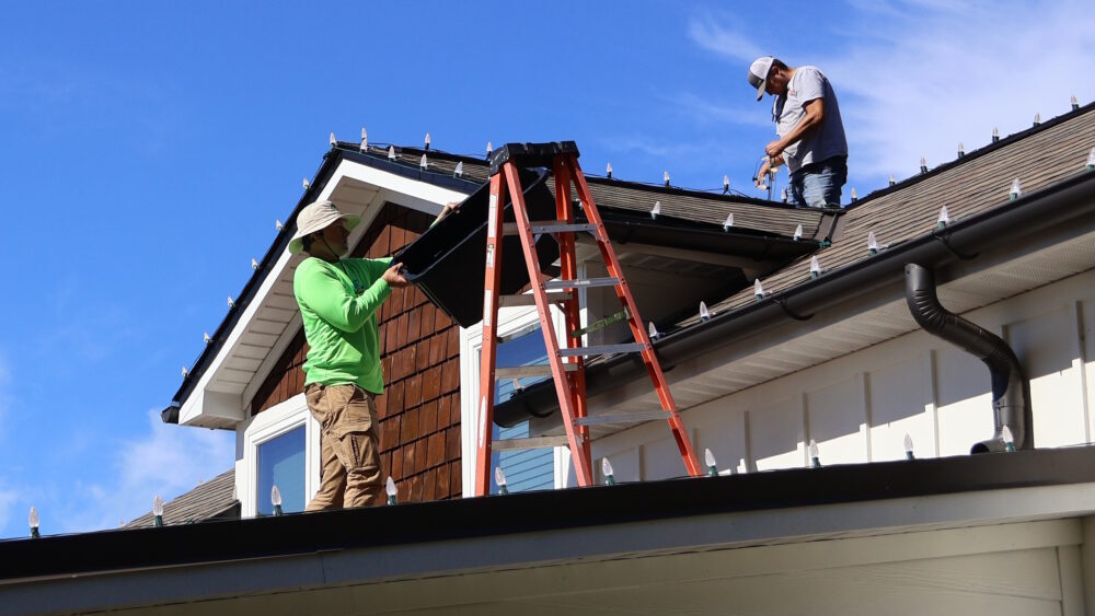 Professional workers performing Christmas light installation on residential roofline using ladder